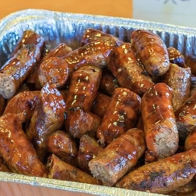 Close-up of a foil pan filled with glistening, brown, cut-up sausages from Kenny's Ribs and Chicken.
